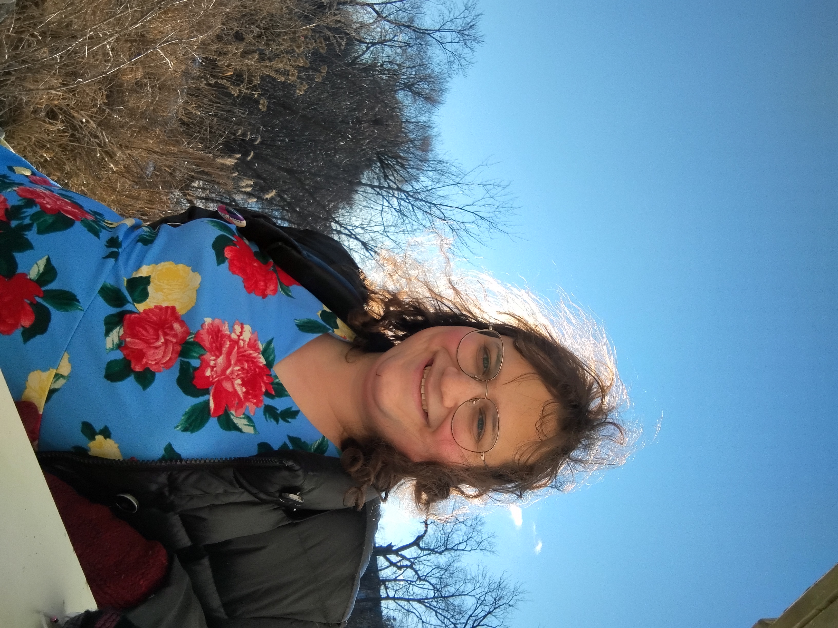 I've opened my jacket to show my dress, blue with big vibrant red and white flowers. The sun is direcly behind my head, glinting through my hair.