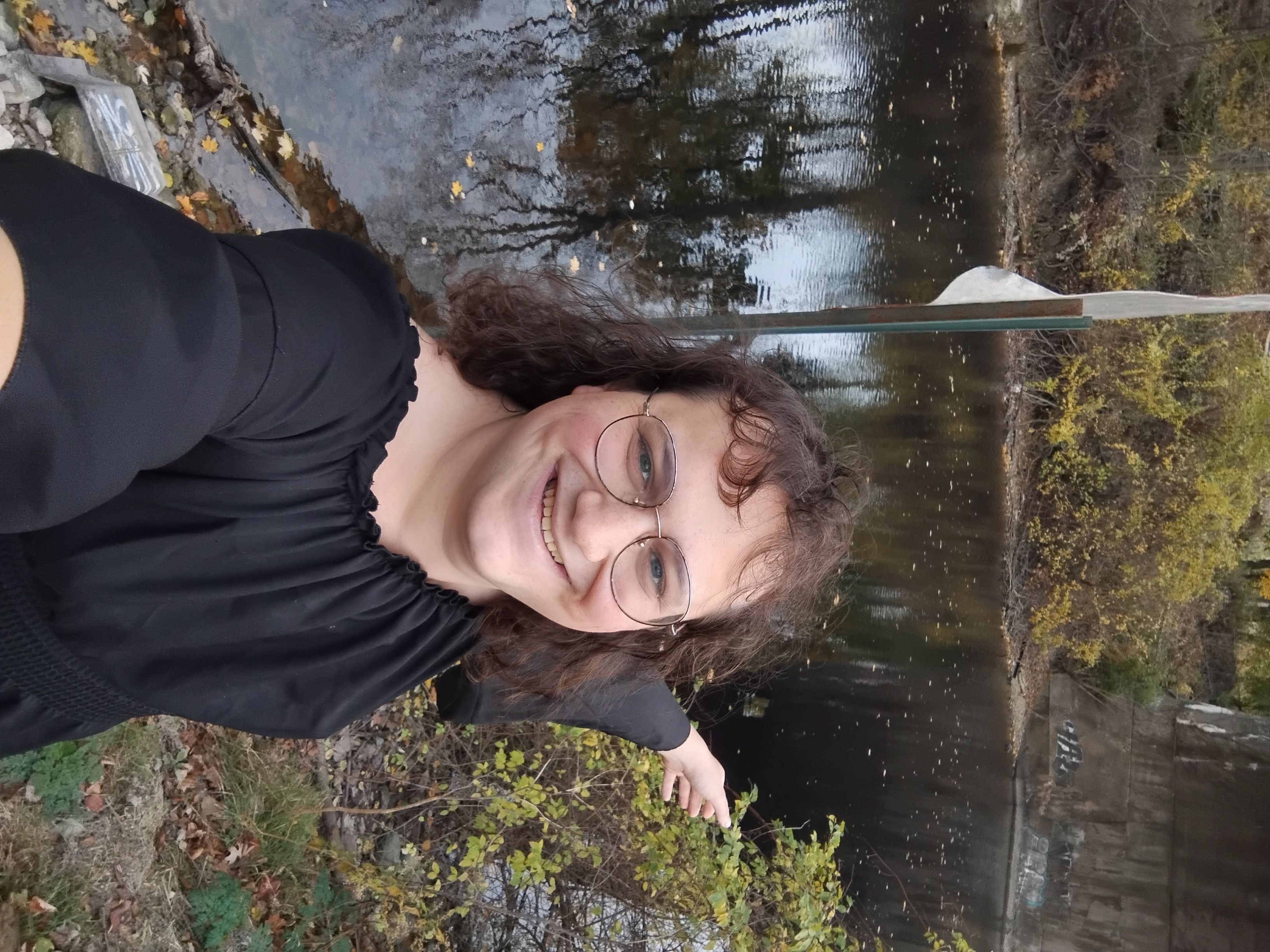 Me in front of the river, arms spread ahead and behind, with the bade of a bridge behind me.