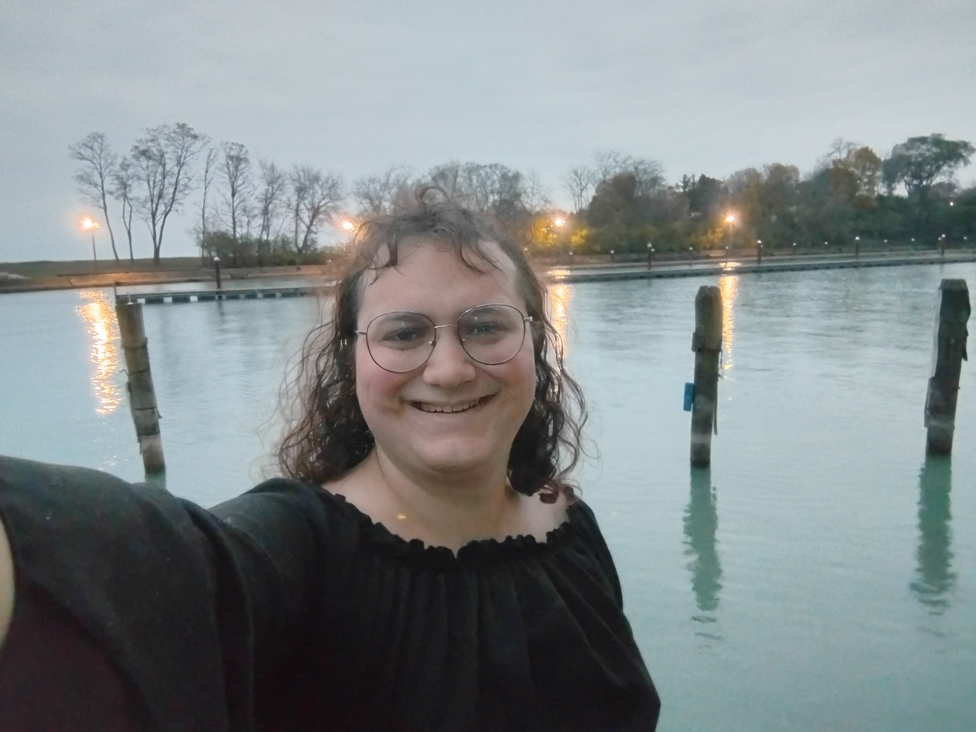 Me in front of the mouth of the river, with a dock and a variety of lights behind me