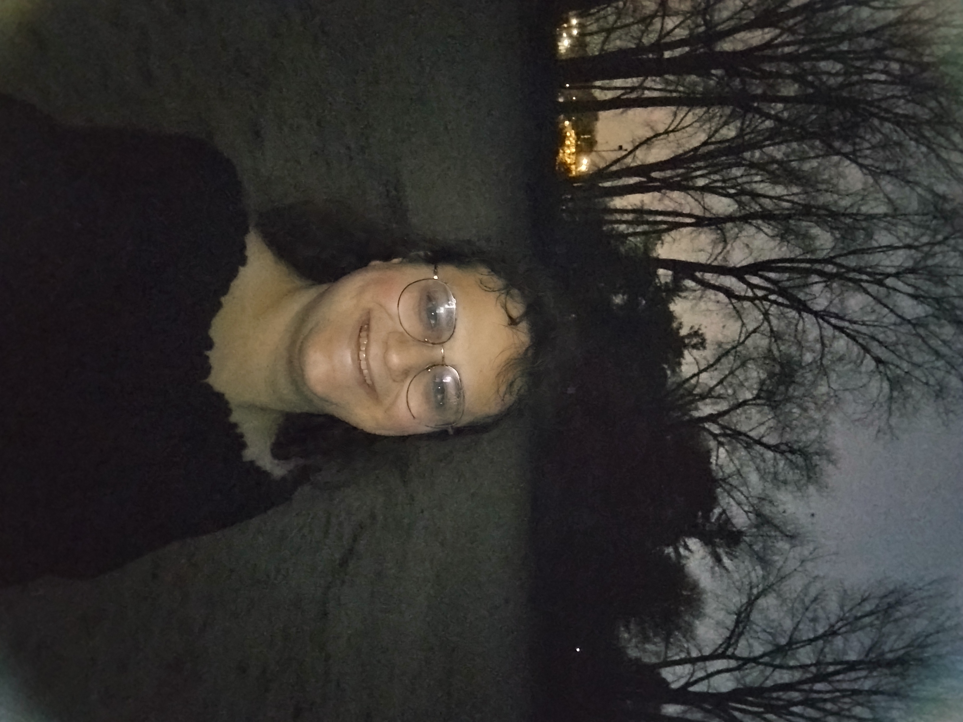 Me at night on the beach, with dark trees and distant lights behind me