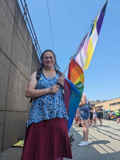 Me at pride, carrying a flagpole with three flags, nonbinary flag at the top